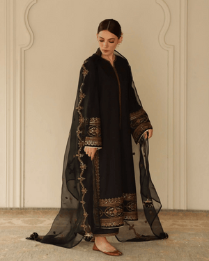 Woman in black embroidered traditional dress with sheer dupatta, standing indoors