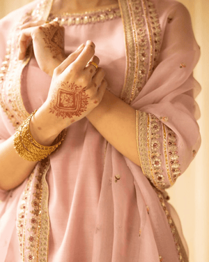 Woman in pink embroidered Indian suit with gold bangles and floral mehendi design