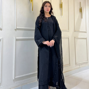 Woman in black embroidered abaya and dupatta standing against white paneled wall