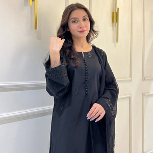 Woman in black embroidered kurta and dupatta posing indoors against cream wall