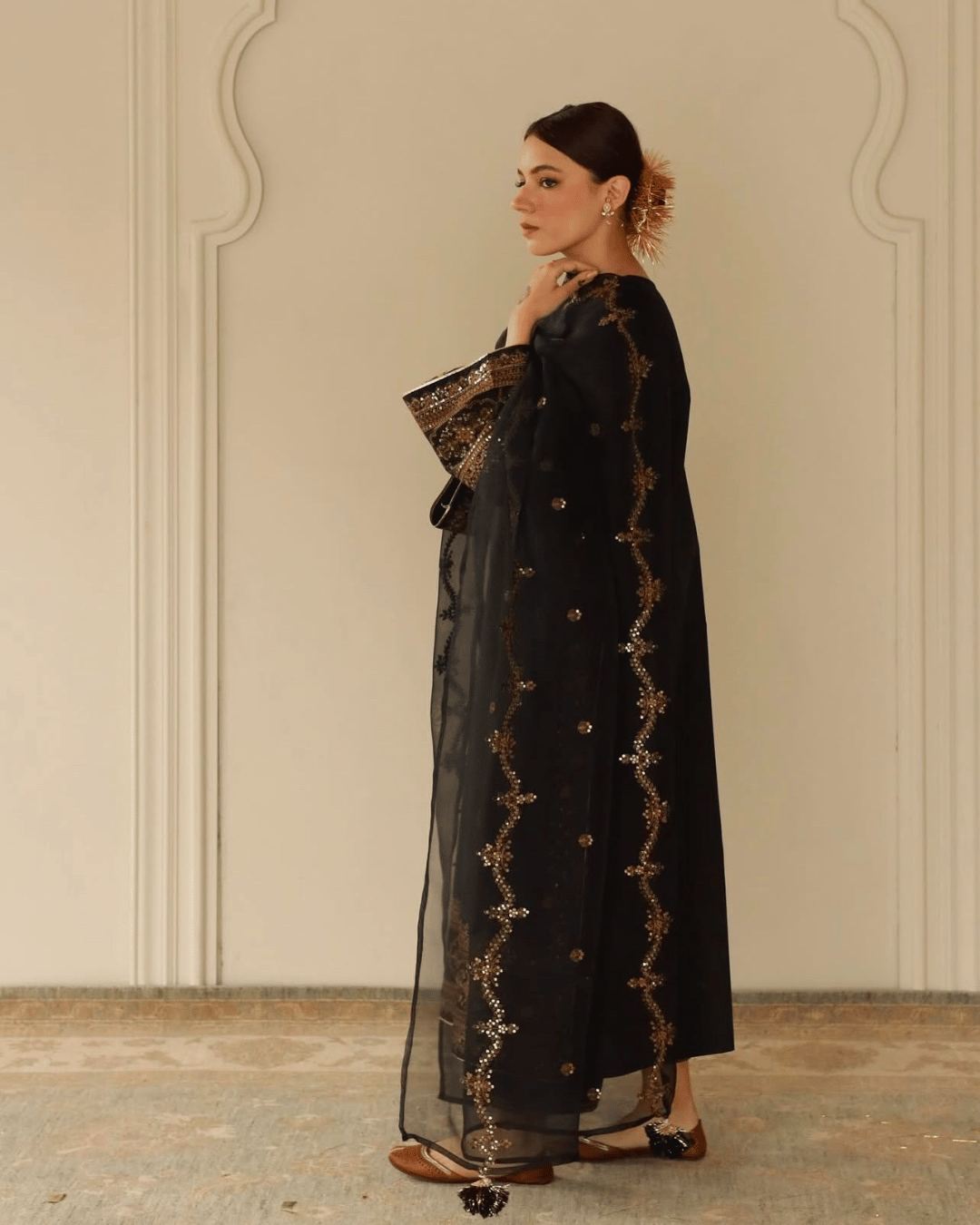 Woman wearing a black embroidered abaya dress with gold details, standing indoors