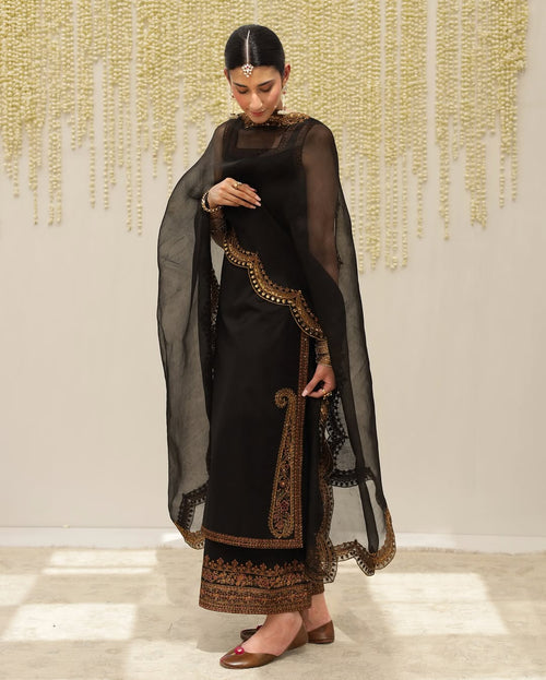 Woman in black embroidered salwar kameez with dupatta, gold jewelry, festive background