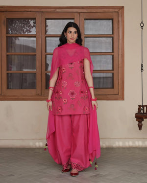 Woman in bright pink floral embroidered Punjabi suit with dupatta, standing indoors