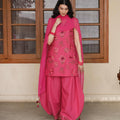 Woman in pink floral embroidered salwar kameez with matching dupatta, standing indoors