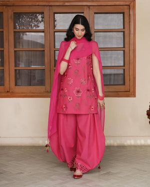 Woman in pink floral embroidered salwar kameez with matching dupatta, standing indoors