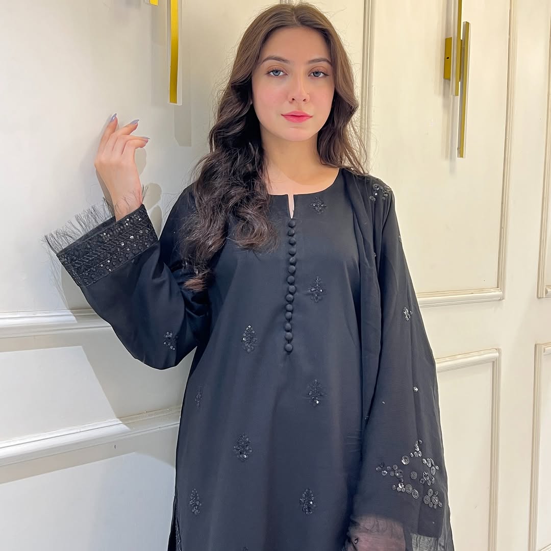Woman in black embroidered kurta with sequin cuffs posing indoors by a cream wall