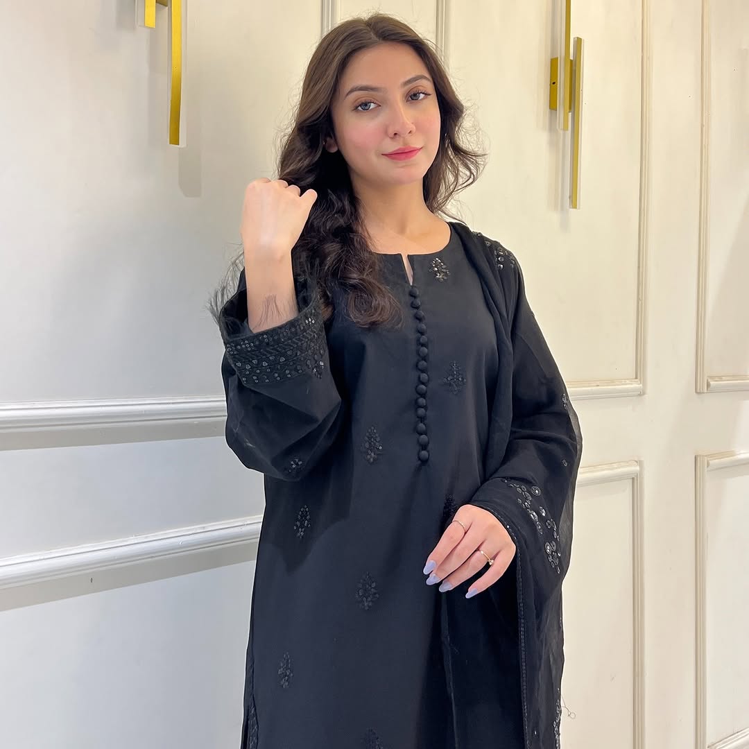Woman in black embroidered kurta and dupatta posing indoors against cream wall