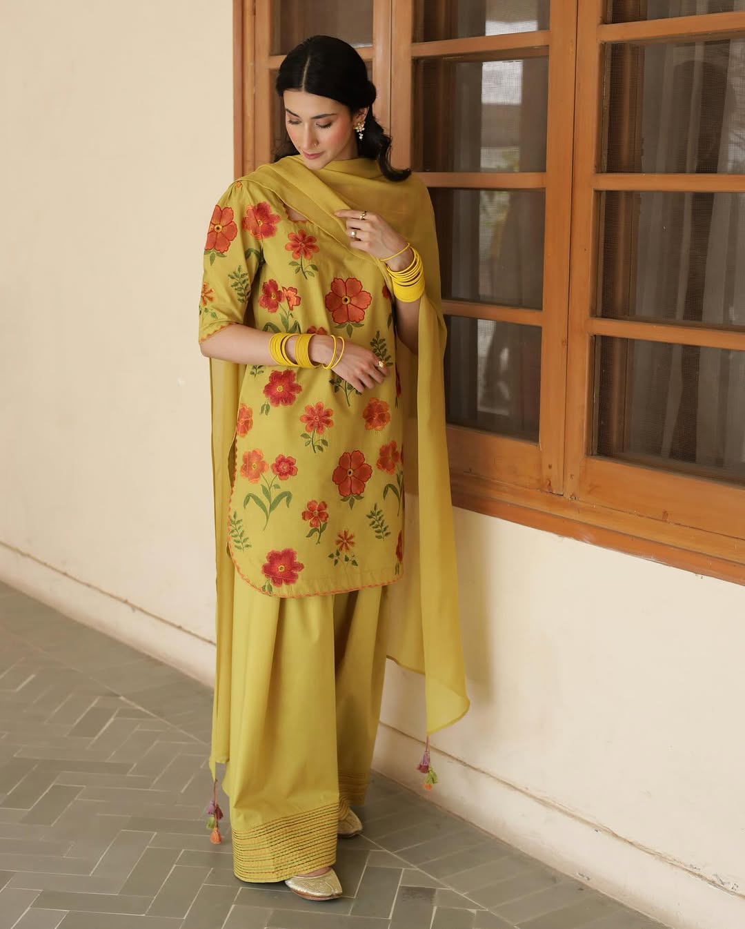 Woman in yellow floral embroidered shalwar kameez standing by window indoors