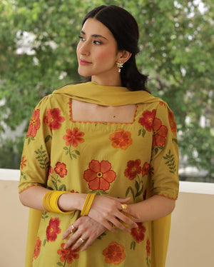 Woman in yellow floral kurta with dupatta and gold jewelry, standing outdoors.
