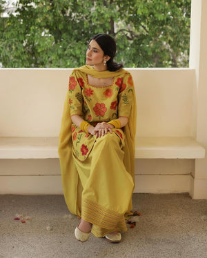 Woman in yellow floral salwar kameez sitting on a bench, trees in background